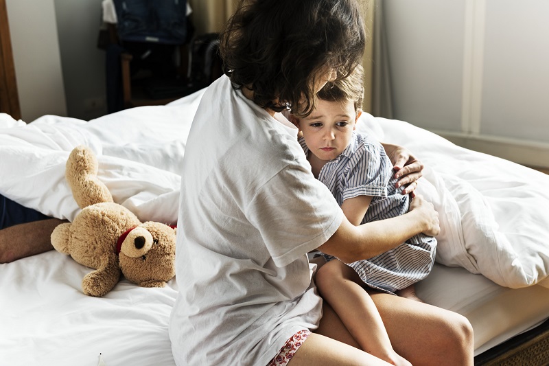 Woman sitting on a bed while holding and comforting a young boy who looks sad. What is positive punishment and how does positive punishment work?